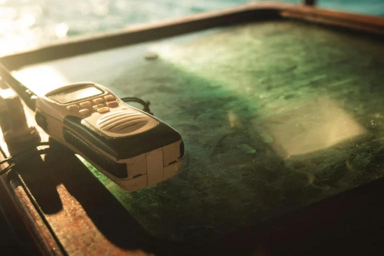 Ręczne radio morskie VHF leżące na drewnianym pulpicie łodzi w promieniach zachodzącego słońca.